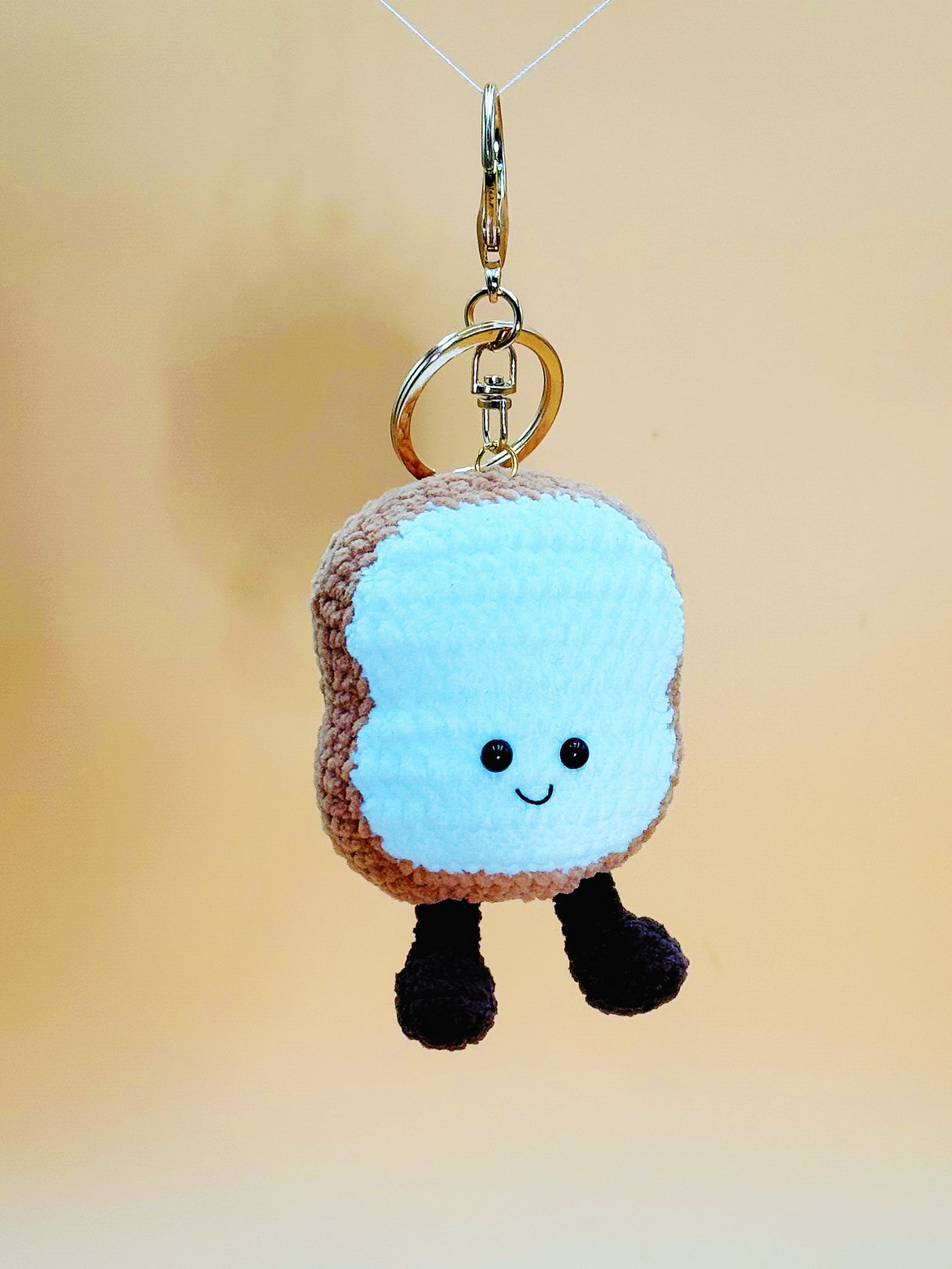 Small plush charm resembling a slice of bread with a face on a plain background