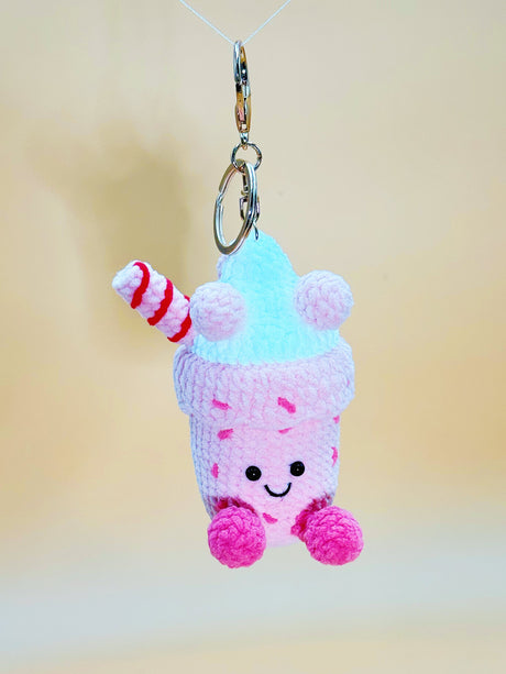 Crocheted milk shake keychain with a smiley face on a plain background